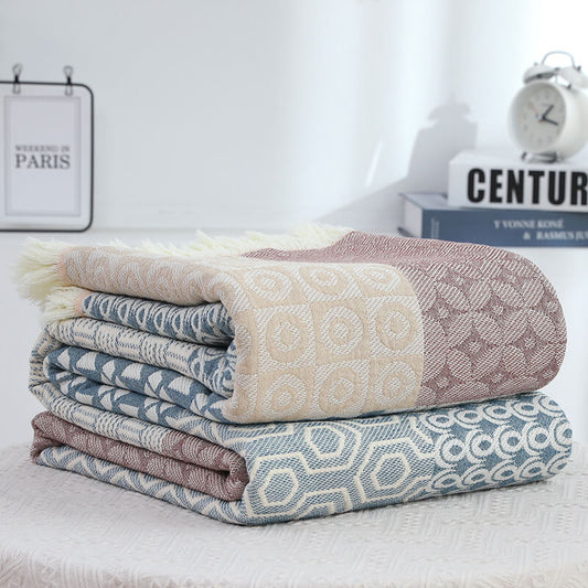 Stack of folded 100% cotton throw blankets featuring a mix of blue, beige, and mauve geometric patterns with soft fringed edges.