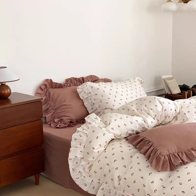 A cozy bedroom scene with an affordable cotton muslin cherry print bedding set; includes ruffled shams and duvet cover with solid dusty rose accents.