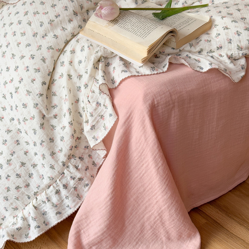 Detail of the Bellflower Floral Cotton Gauze Duvet Cover with ruffle trim, draped next to a solid pink cotton sheet that highlights the contrasting color and the double gauze texture.