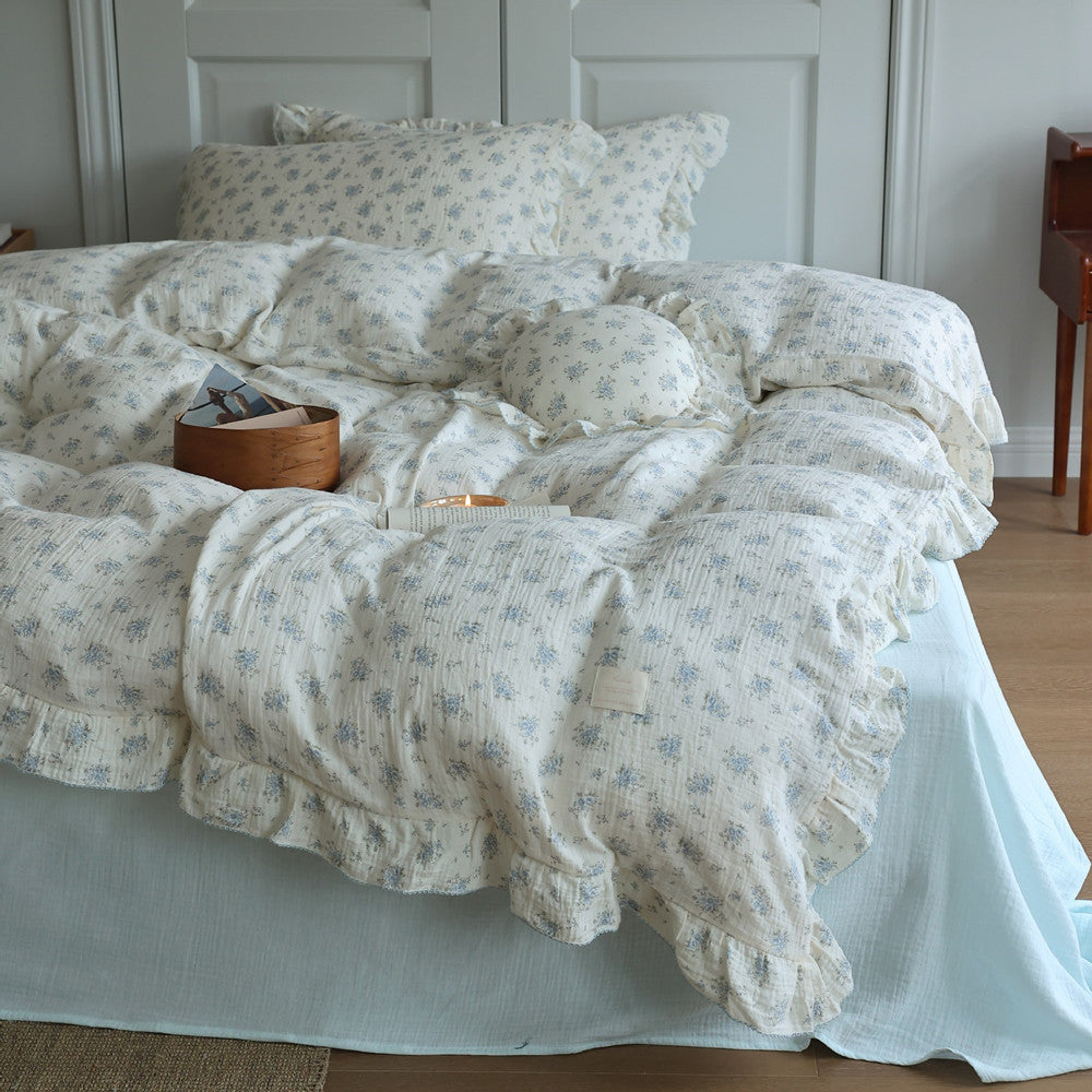A stylized shot of a bed showing a blue floral cotton muslin ruffled duvet cover set and a matching round cushion.