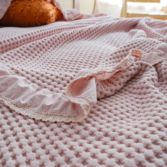 Macro shot of the breathable woven texture and delicate lace trim on a pink waffle blanket.