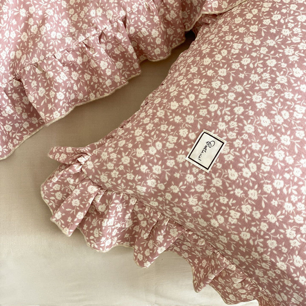 Macro detail of the pink ditsy floral pillow, showcasing the cotton muslin texture, the small print, and the brand label near the ruffled edges.