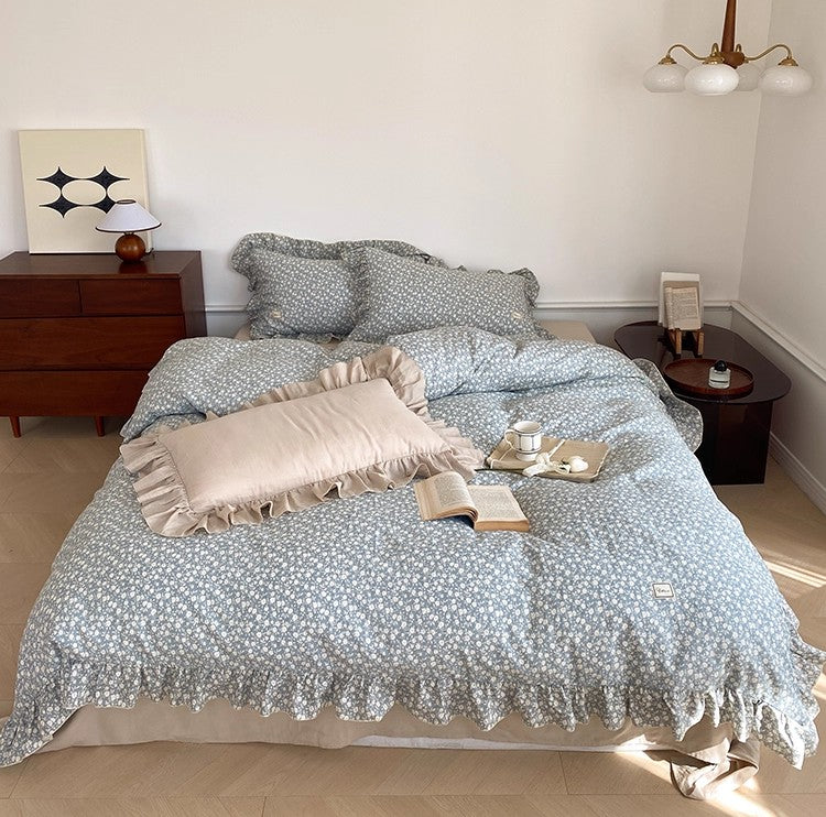 Full bed view of the blue ditsy floral bedding set, highlighting the cotton muslin texture and the contrasting solid ruffle pillow.