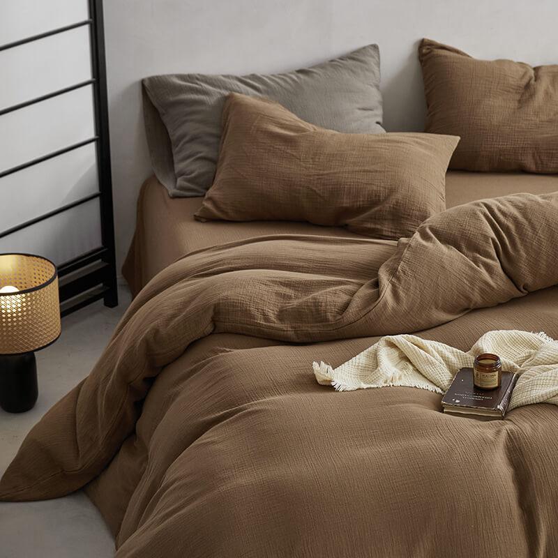 Brown bedding set on a bed with a lamp and books on a nightstand.