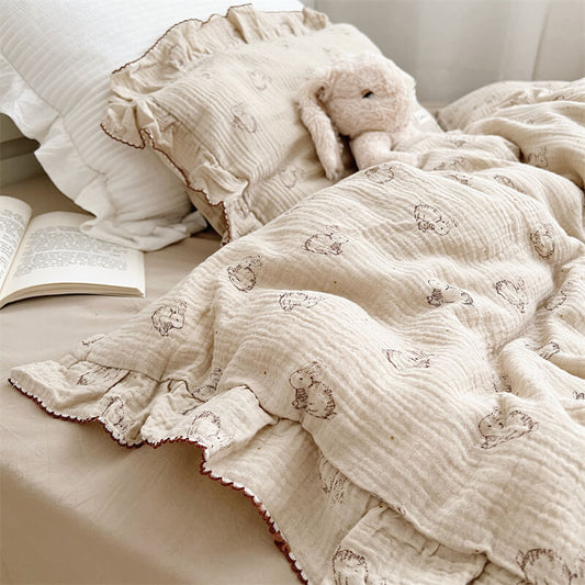 A side-angle view of a twin-size muslin bed set featuring a whimsical bunny print and a solid-colored flat sheet. The bedding has a relaxed, lived-in feel with soft ruffles along the edges.
