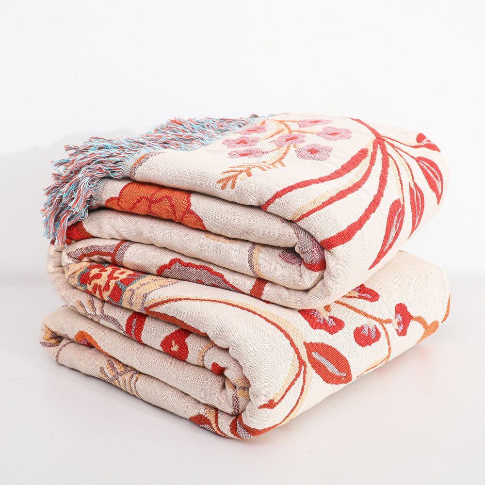 The jacquard cotton throw blanket folded neatly in a stack of two, revealing the large-scale floral design in red, orange, and beige. The multi-colored fringe is visible on the top edge of the stack.