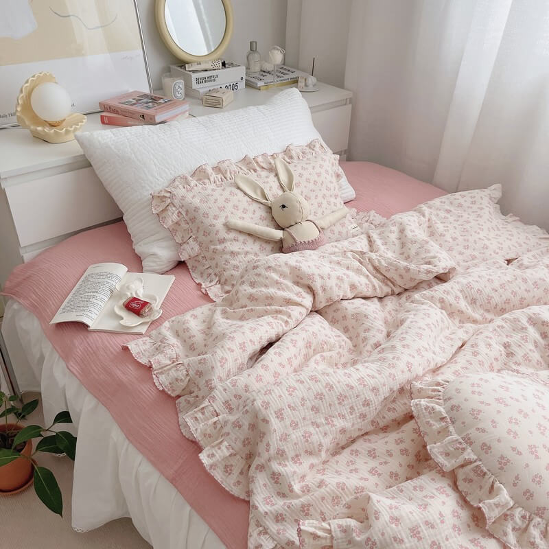 A twin-size bed featuring a pink dainty floral cotton muslin duvet cover set with a matching ruffle pillow and a stuffed bunny toy. The bedding has a soft, romantic look, complementing the solid pink bed sheet and a white quilted pillow. The overall aesthetic is perfect for a girl's bedroom.