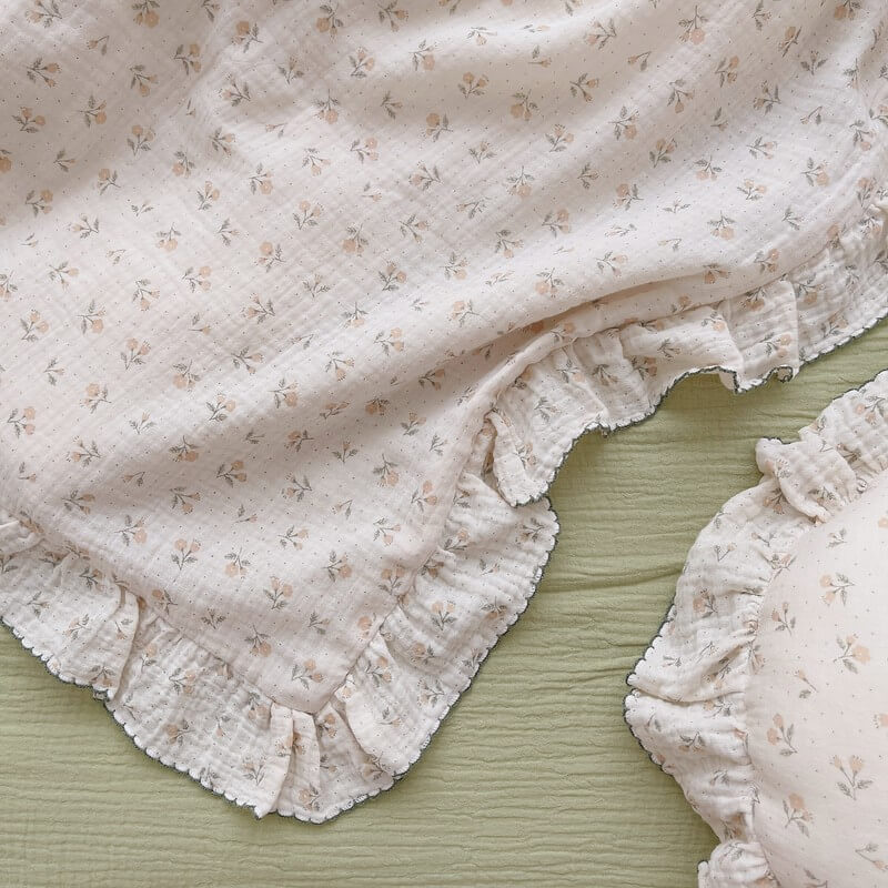 An overhead shot of a high-quality ruffle bedding set, showcasing the intricate floral print and the ruffled edges with contrasting dark stitching. The bedding is placed on a light green base, highlighting the soft, breathable texture of the cotton gauze duvet cover.