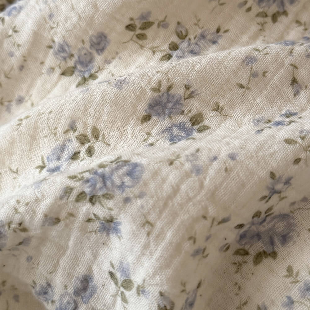 Close-up of cotton linen fabric with soft blue rose floral print and muted green leaves