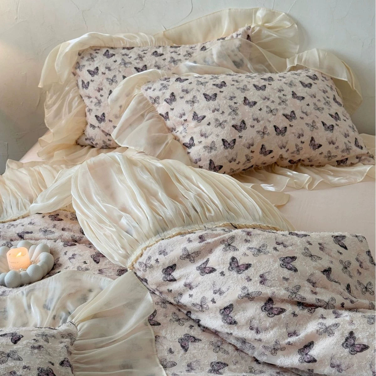 Butterfly-patterned bedding set on a bed with a candle in the corner.