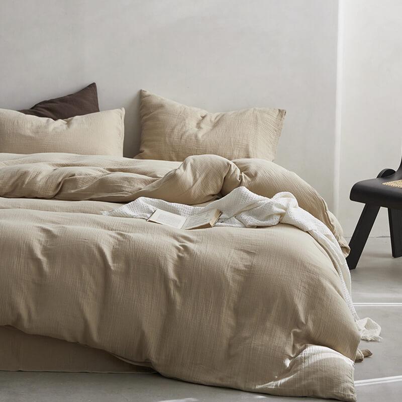Beige bedding set on a bed with pillows in a minimalistic room.