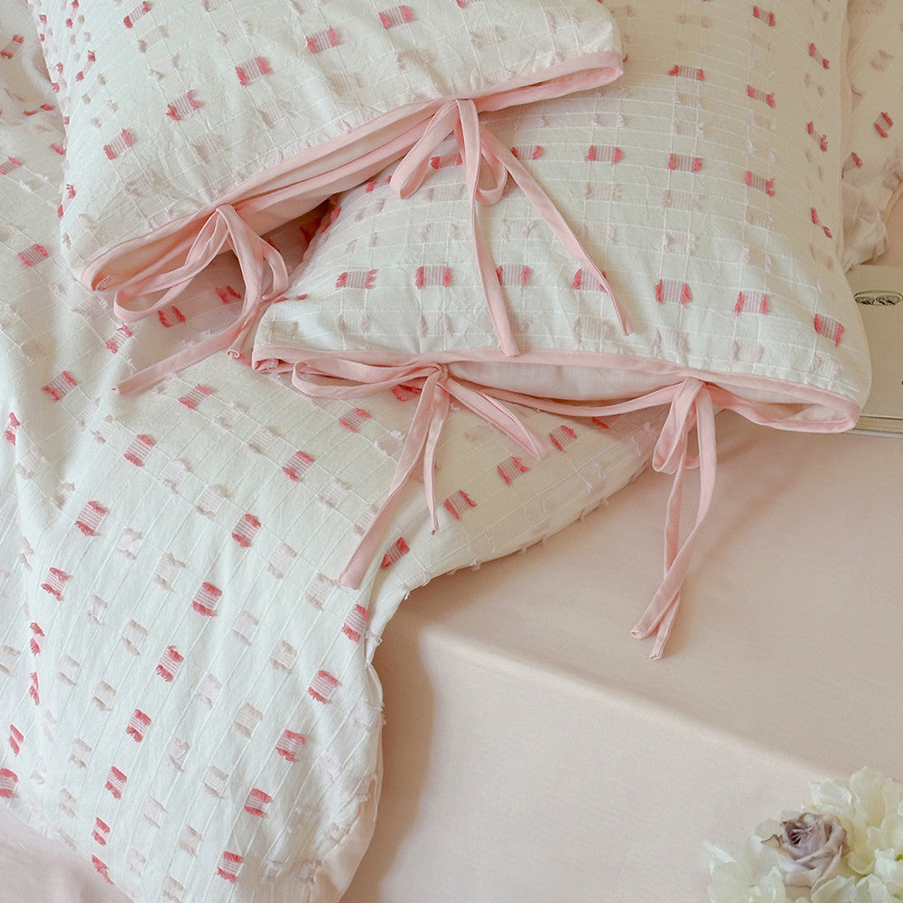 Macro close-up of the Tufted Check pattern on the cotton fabric, detailing the pink tufts and the ribbon ties on the pillow sham closure, emphasizing high-quality finish and texture.