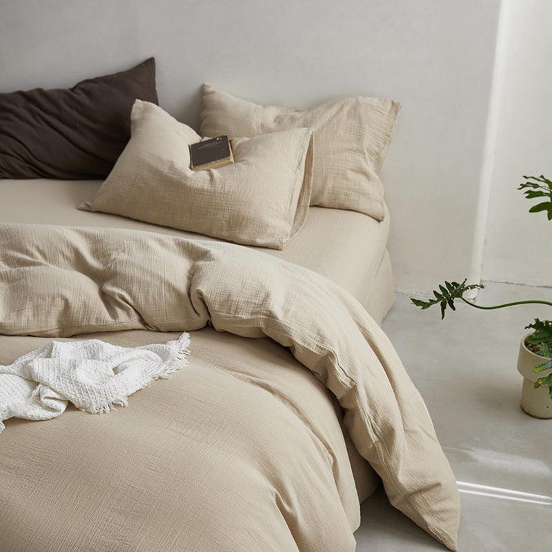 Beige bedding set on a bed with pillows and a plant in the corner.