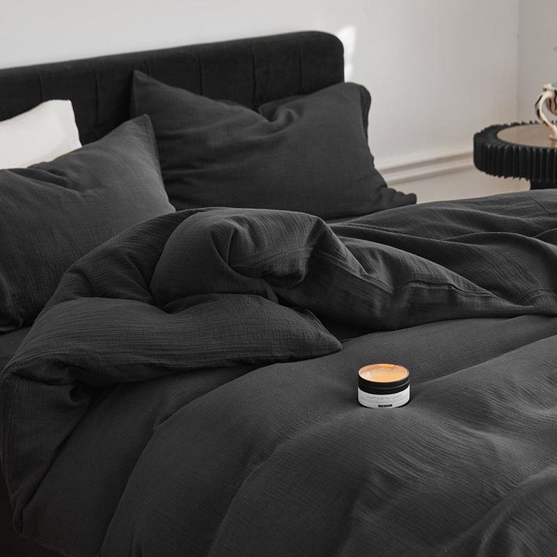 Dark gray bedding set on a bed with a small candle on top, in a minimalistic room.