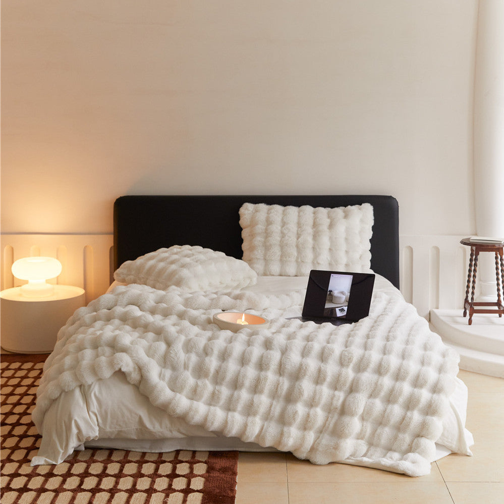 An eye-level view of a bed with a white faux rabbit fur blanket draped over it, featuring a prominent bubbly texture.