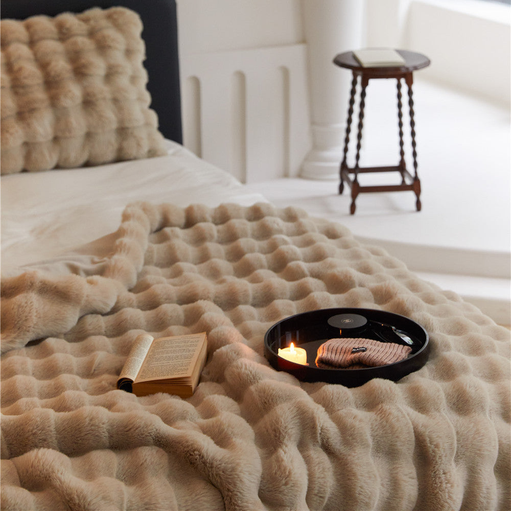 A close-up of a tan-colored faux rabbit fur throw blanket with a plush, grid-like pattern, laid out on a bed.
