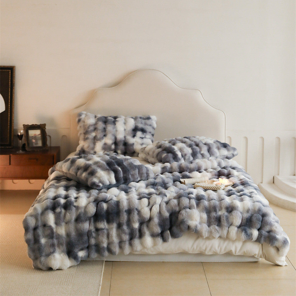 A bed covered with a gray and white tie-dye patterned faux rabbit fur blanket and matching pillows, showcasing its soft and luxurious texture.