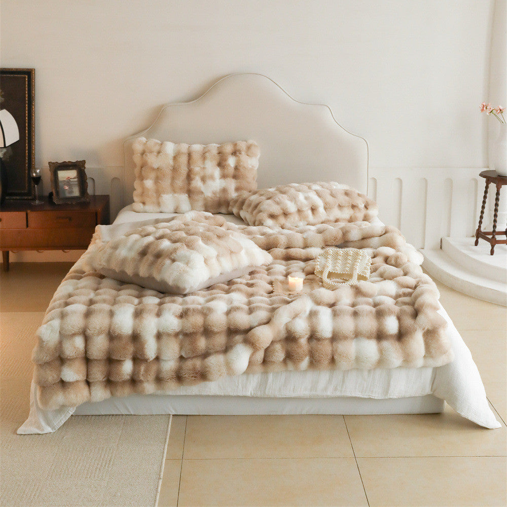 A full view of a bed with a light brown and white tie-dye patterned faux rabbit fur blanket and multiple matching pillows, creating a cozy and luxurious look.