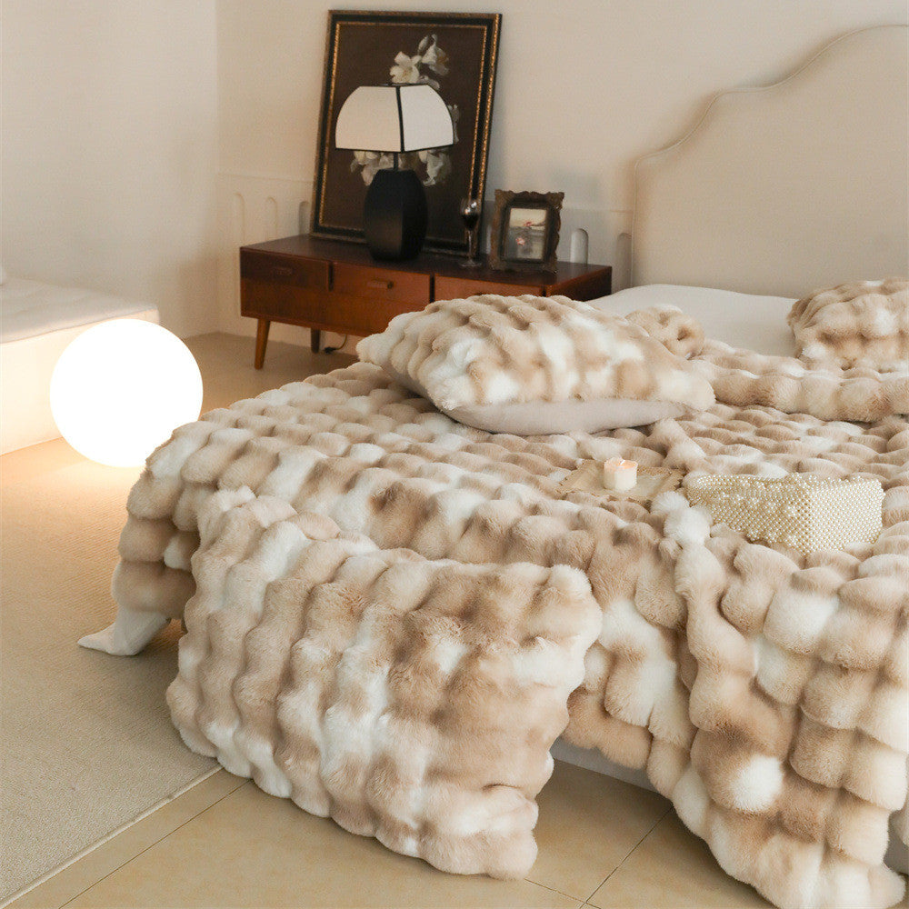 A bed with a light brown and white tie-dye faux rabbit fur blanket and matching pillows, showcasing its plush texture.