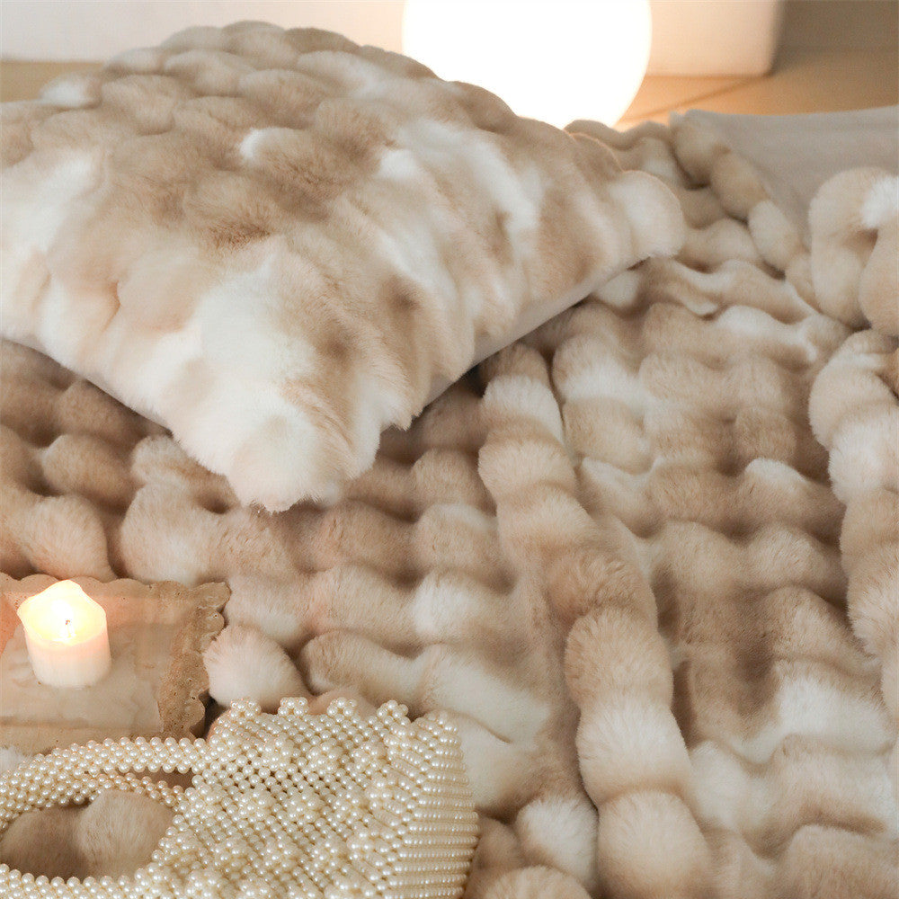 A close-up shot of a light brown and white tie-dye faux rabbit fur blanket and a matching pillow, highlighting the fluffy texture.