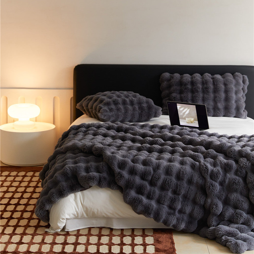 An eye-level view of a bed with a Charcoal faux rabbit fur blanket and matching pillows, featuring a bubbly texture.