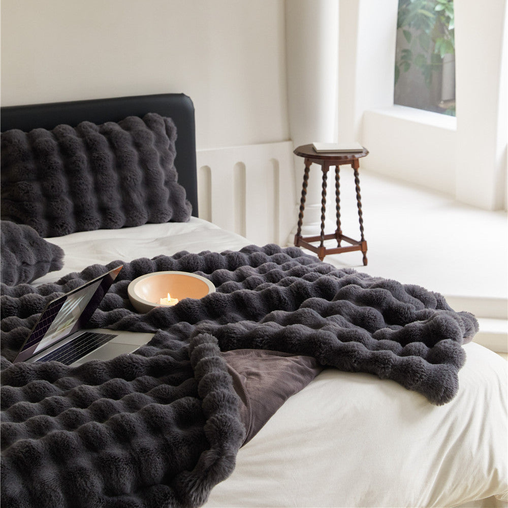 A Charcoal faux rabbit fur throw blanket with a bubble texture, draped over a bed with a matching pillow.