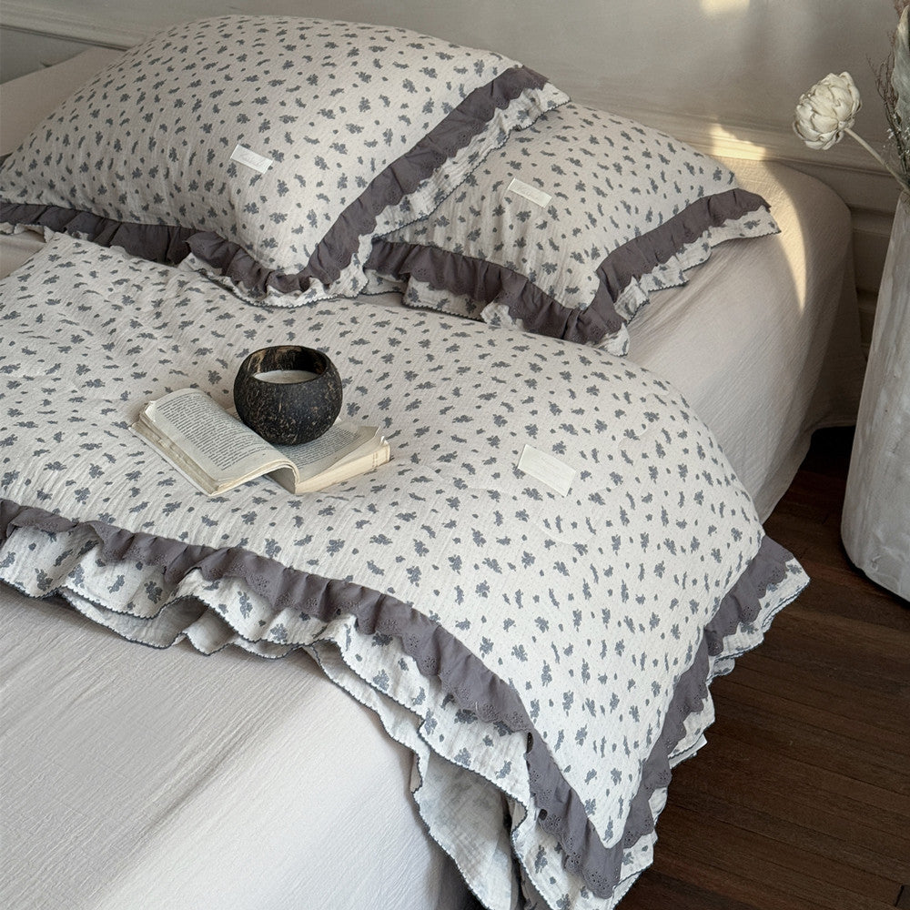 Bed with floral-patterned bedding and ruffled edges, featuring a book and candle.