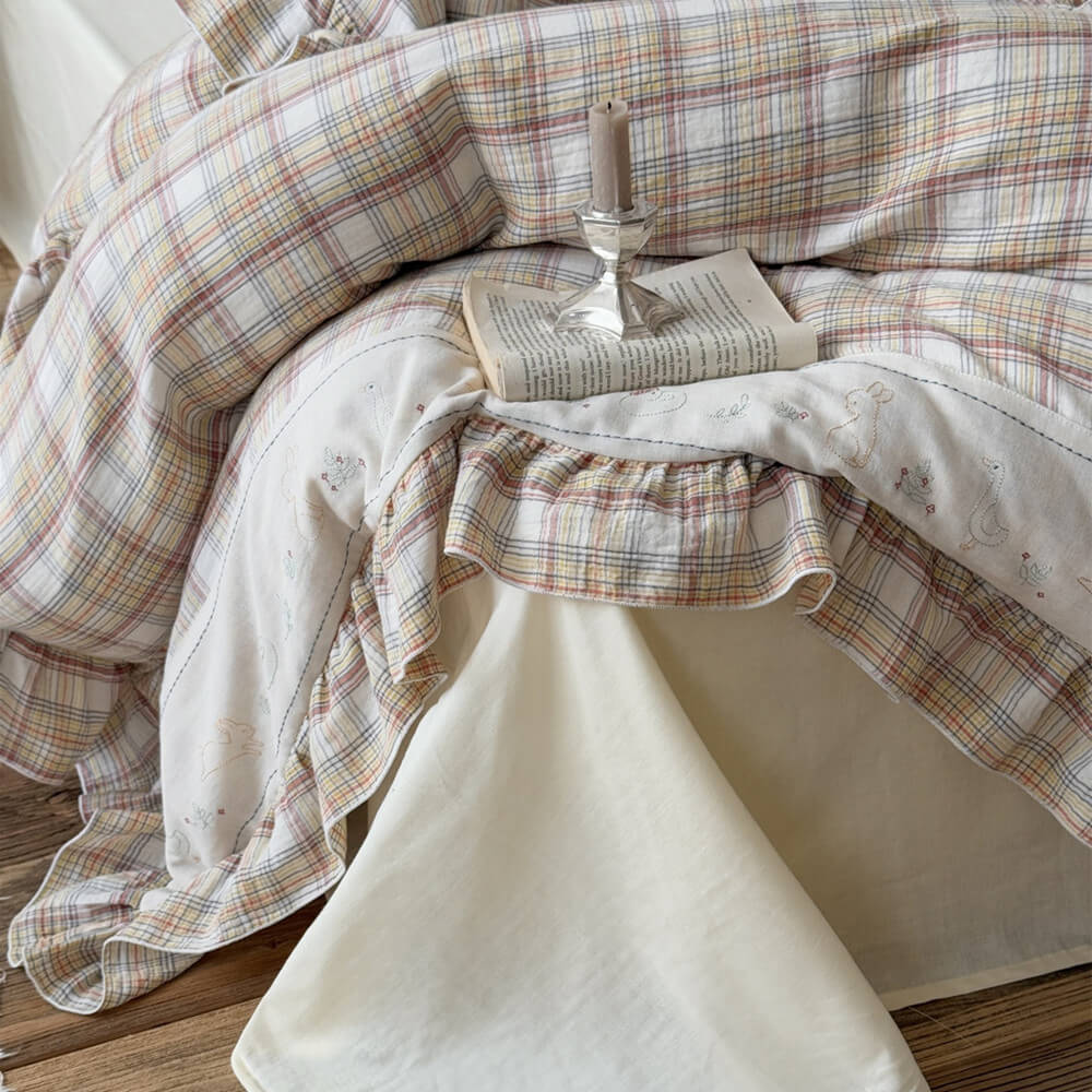 Detail of beige plaid ruffle duvet cover with embroidery, paired with a cream cotton flat sheet