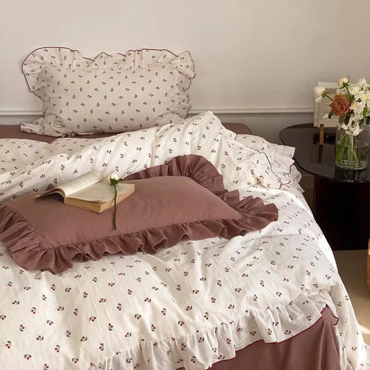 A bed with soft cotton bedding set featuring a duvet cover, flat sheet, and two pillowcases with a cherry print and ruffles.