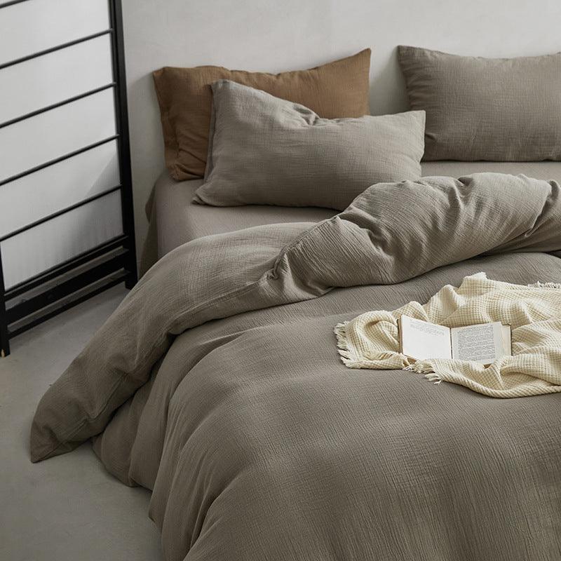 Bed with brown bedding and pillows, featuring a blanket and book on a wooden floor.