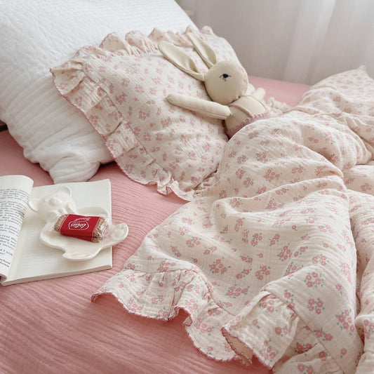 An overhead view of a pink dainty floral muslin bedding set on a bed. The image shows the soft, crinkled texture of the fabric, the ruffle detailing on the duvet cover and pillowcase. This is a cozy shot of a twin comforter set for a girl.