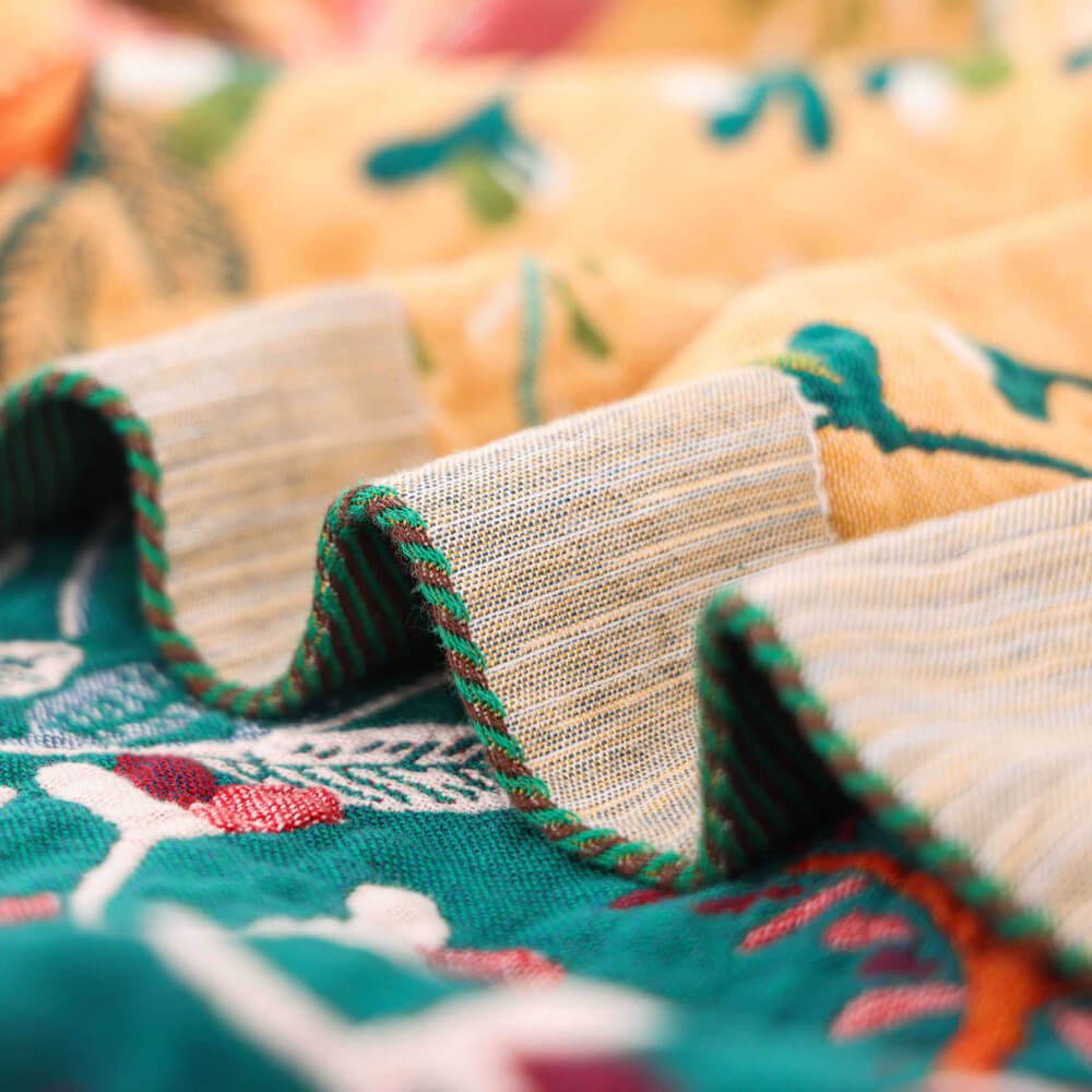Detailed shot of the green ribbed border and soft folds of a reversible cotton botanical throw blanket.