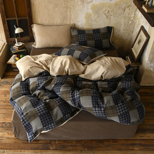Plaid blanket and pillows on a bed in a cozy room with wooden floor and rustic decor.