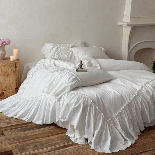 White cotton bedding set with ruffled trim on a cozy bed in a rustic bedroom setting