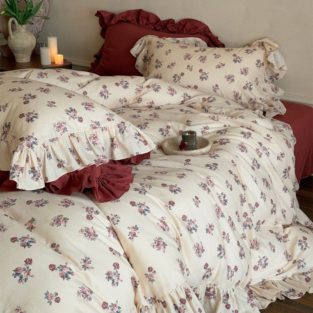 An elegantly styled bed featuring the Ruffled Cotton Design with a dense vintage rose floral print and deep red solid pillows for contrast.