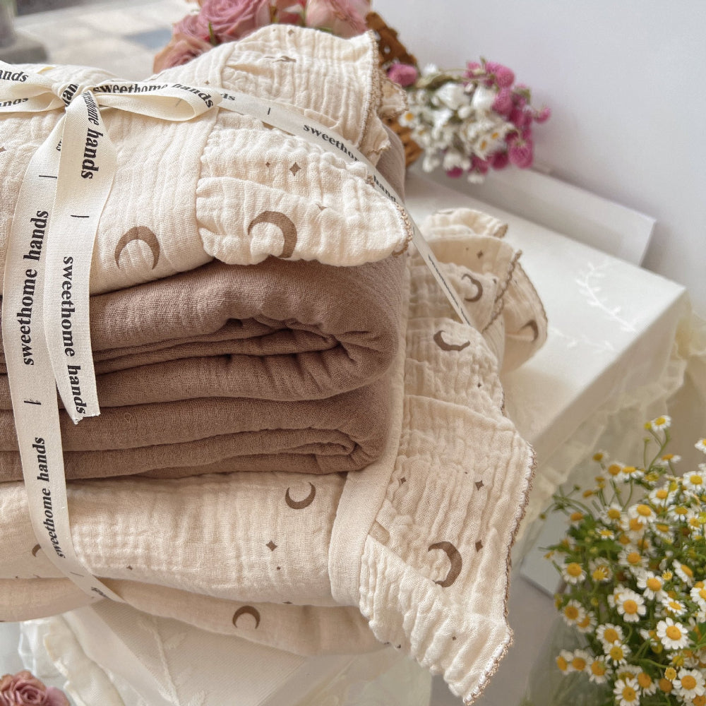 Folded twin bedding set with a cotton gauze duvet and pillow shams tied with a ribbon, ready for gifting. Shows the moons and stars print.