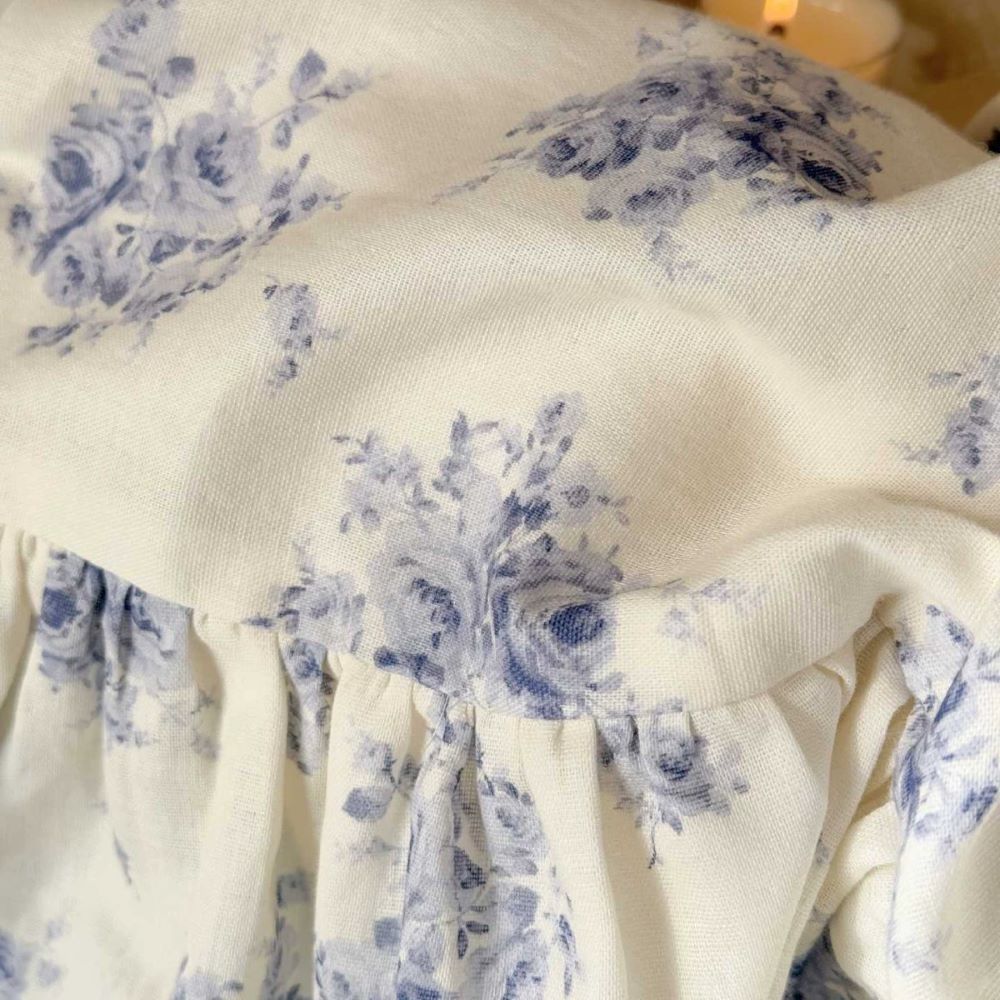 Close-up: Blue rose floral print and ruffled border detail on off-white cotton fabric.