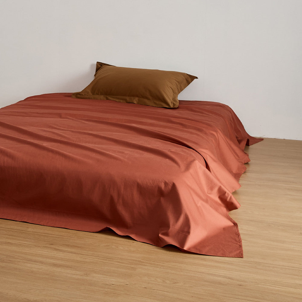 A Rust-colored flat sheet from the Brushed Cotton Duvet Cover Set draped on a bed.