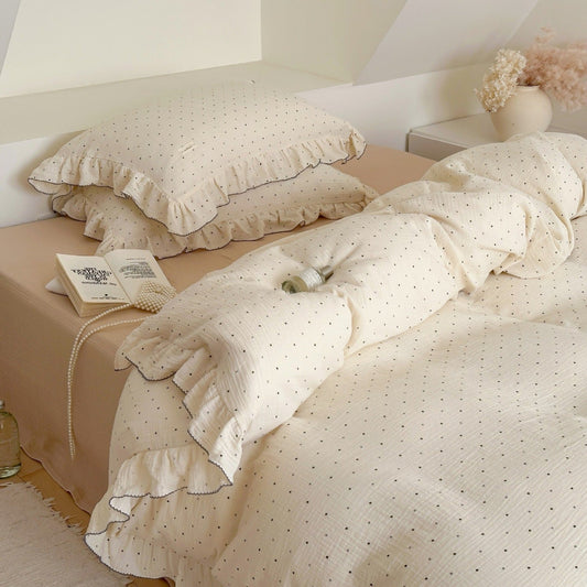 Soft cotton muslin duvet cover set featuring a polka dot pattern and ruffled design, styled on a bed with a book and pearl necklace.