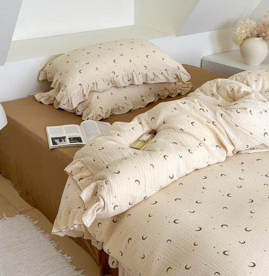 Twin-size cotton gauze duvet cover set with moons and stars print. Includes a duvet and two ruffled pillow shams on a bed.