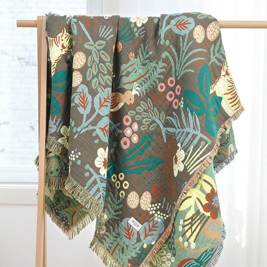 Full view of a jungle-themed cotton woven blanket with fringe, hung on a wooden display rack.