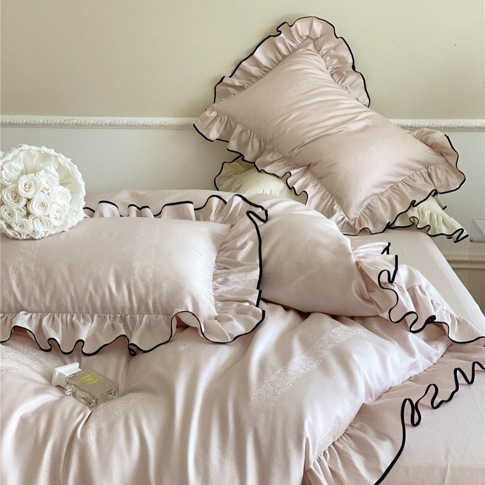 Bed view of the delicate ruffle bedding set in light pink, highlighting the shiny satin sateen material and the elegant black piped edge.