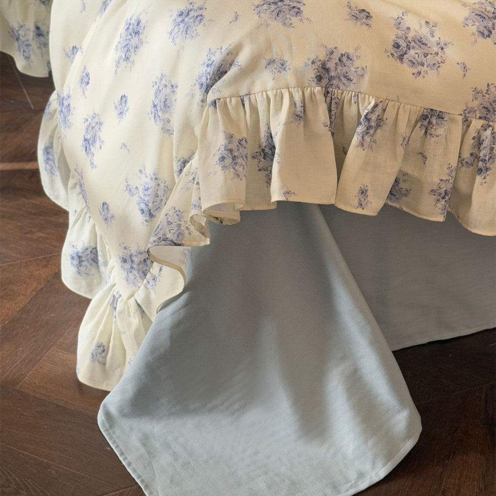 Bottom detail: Ruffled blue rose duvet cover edge draping over a dusty blue flat sheet.