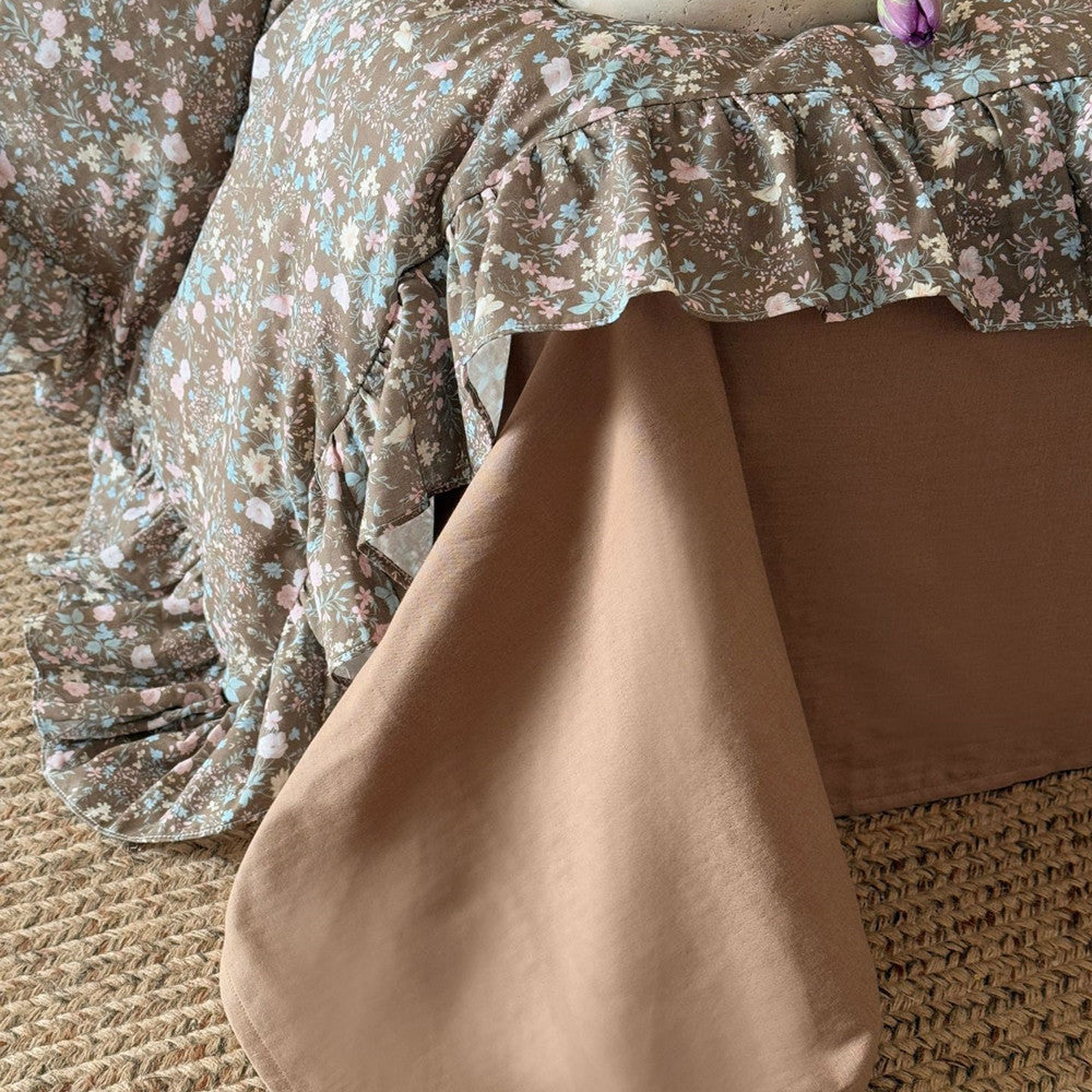 Detail showing the corner of the Earthy Floral Bedding Set and the solid brown fitted sheet/bed skirt underneath, with the duvet's ruffled border.