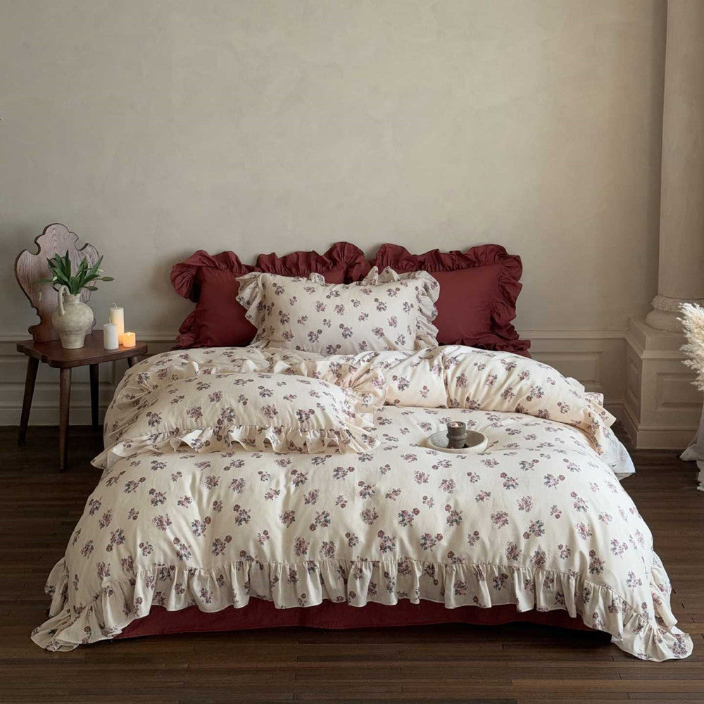 Full view of a Vintage Rose Floral Bedding Set on a bed, showing the ruffled cotton duvet and shams with a red fitted sheet and matching accent pillows.