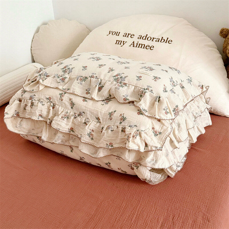 A side-angle view of a bed with a floral cotton duvet cover, showcasing the relaxed, crinkled texture of the muslin gauze. The bedding has a ruffled edge with dark piping, and is paired with a matching pillow, creating a cozy and inviting bedroom look.