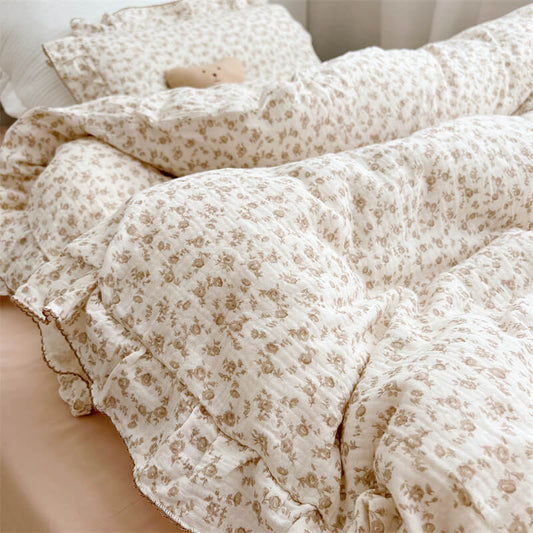 An overhead view of a twin bed featuring a brown camellia floral duvet cover set with a matching pillow. The cozy, casual aesthetic is emphasized by the soft folds of the muslin fabric and a stuffed toy next to the pillow.