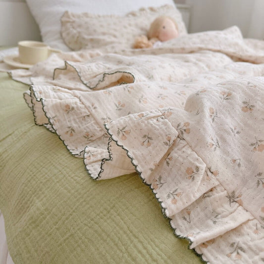A close-up side-angle shot of a floral ruffle duvet cover draped on a bed. The image highlights the detailed, scalloped ruffled edge with dark piping and the subtle floral pattern. The light green flat sheet below creates a fresh, natural aesthetic.