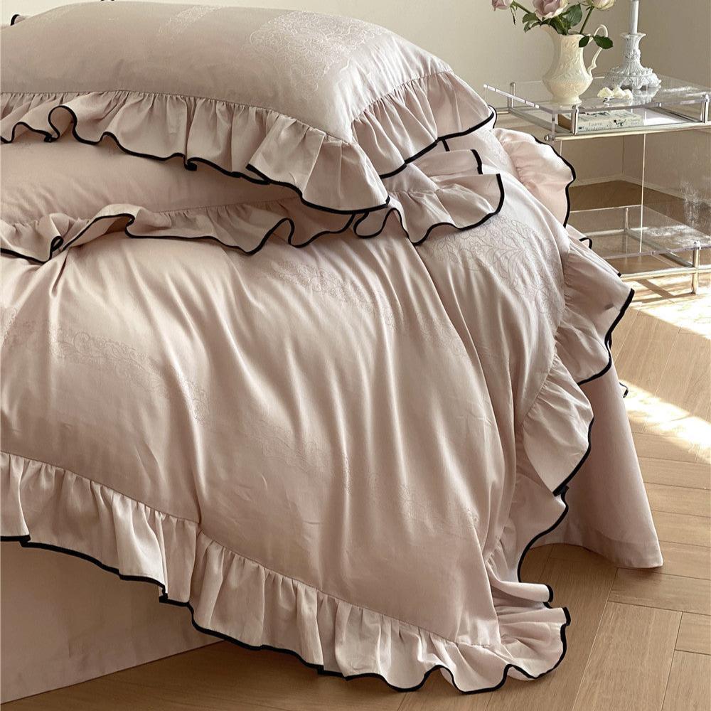 Angled close-up of the frilly ruffle bedding set in light pink with black trim, showing the smooth texture and layered duvet cover.