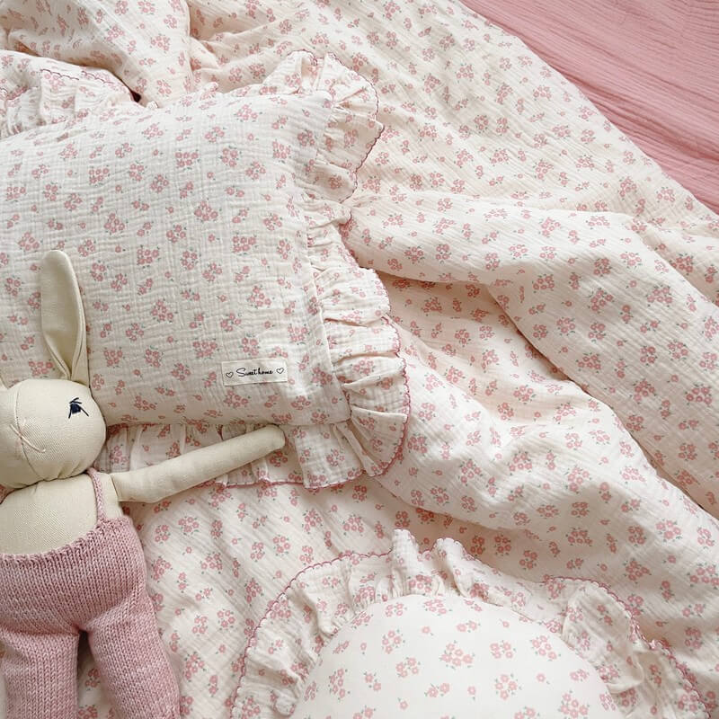 A close-up shot of the pink dainty floral duvet cover set on a bed, showing the intricate floral pattern and the detailed ruffled edges with a stitched pink border. A stuffed bunny toy rests on the matching pillow, highlighting the whimsical and cozy design.